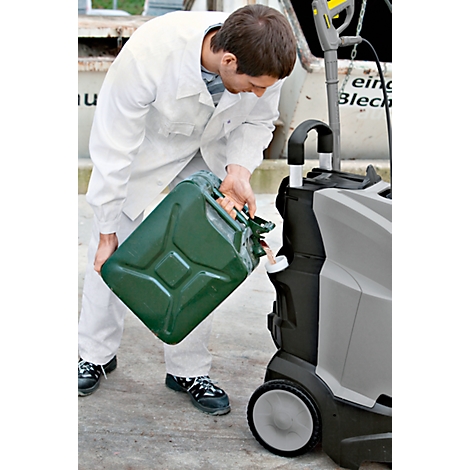 A man in white work clothes pours liquid from a green canister into a cleaning device. The background is blurred.