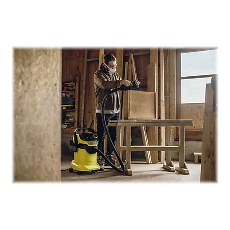 Ein Handwerker schleift in einer Holzwerkstatt ein Möbelstück ab, während ein gelber Kärcher-Industriesauger den Staub direkt absaugt.