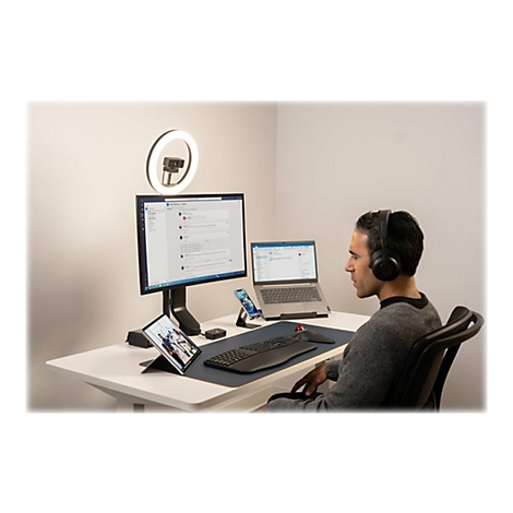 Un homme portant un casque est assis Ã  un bureau avec un Ã©cran, un ordinateur portable, une tablette et une lampe annulaire.