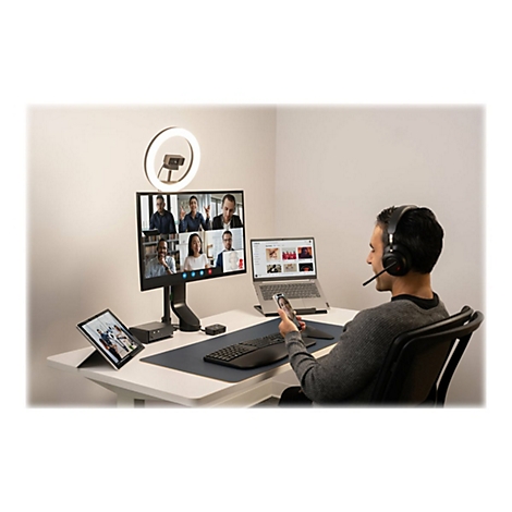 Un homme avec un casque participe Ã  une vidÃ©oconfÃ©rence. Sur le bureau : Ã©cran, tablette, ordinateur portable, anneau lumineux.