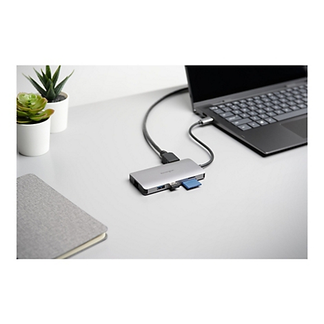 Hub USB-C argentÃ© connectÃ© Ã  un ordinateur portable, Ã  cÃ´tÃ© d'un bloc-notes et de plantes.