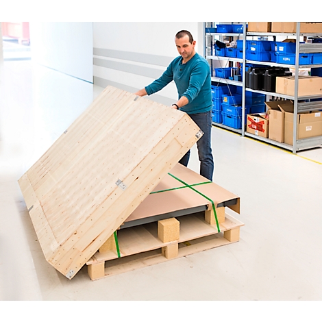 Un homme ouvre une caisse en bois sur une palette. La caisse est fixée avec des sangles vertes, des étagères en arrière-plan.