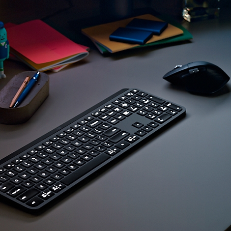 Black illuminated keyboard on a grey desk. A mouse on the right, with notes and pens next to it.