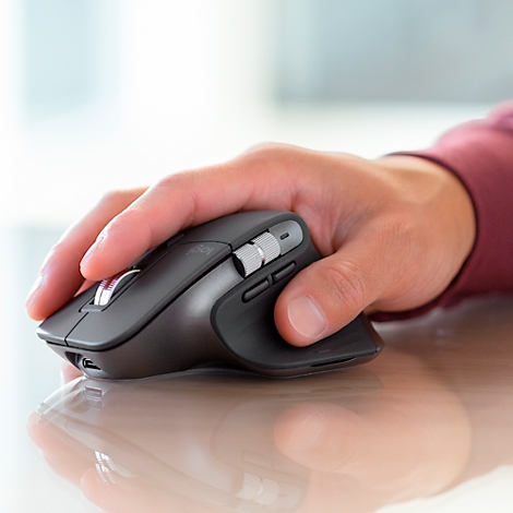 A hand holding a gray computer mouse resting on a light-colored surface.