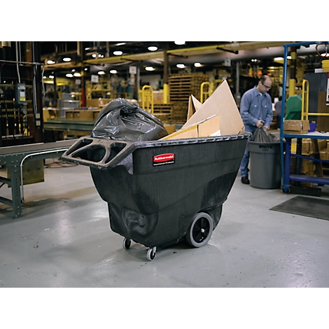 Zwarte industriële afvalwagen, gevuld met vuilniszakken en kartonnen dozen, in een fabriek. Een man sorteert afval.