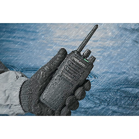 Une radio Kenwood noire est tenue dans une main gantée et mouillée. Il pleut abondamment.