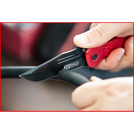 Nahaufnahme eines roten Klappmessers, das ein schwarzes Kabel durchschneidet. Auf der Klinge steht 'KSTOOLS'.