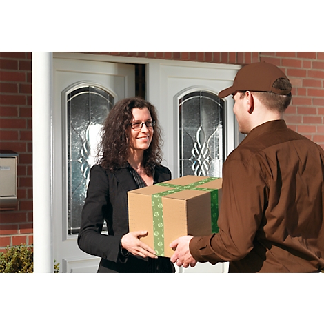 Eine Frau in schwarzer Jacke empfängt ein Paket von einem Zusteller. Beide lächeln. Das Paket ist braun mit grünem Band.