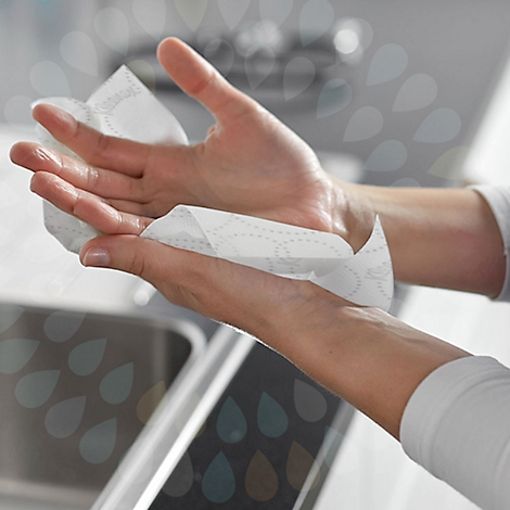 Hände trocknen sich mit Papiertüchern. Eine Hand hält das Papier, die andere wischt die Hände ab.