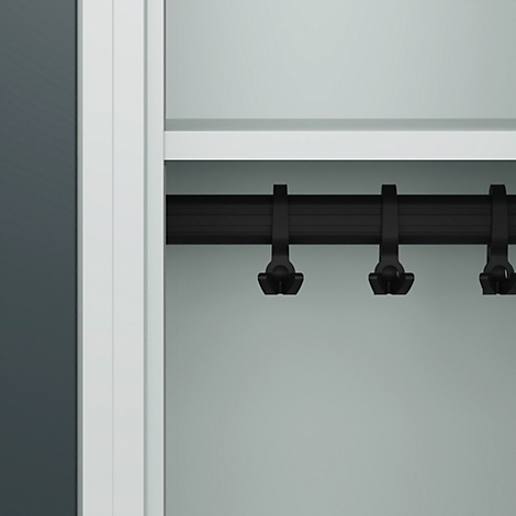Schwarze Haken an einer Stange, in einem weißen Schrank. Graue Wand.