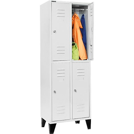 Weißer Spind mit schwarzem Gestell, eine Tür ist geöffnet. Orangefarbene Jacke und blauer Mantel hängen. Grüne Tasche liegt drin.