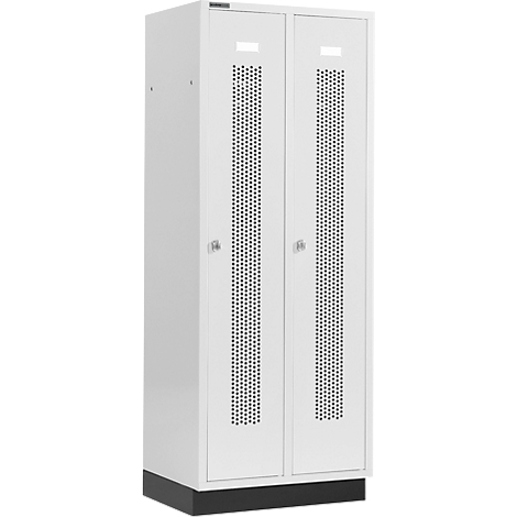 Weißer Doppelschrank mit Lochmuster in den Türen und kleinen Griffen. Der Schrank steht auf einem schwarzen Sockel.