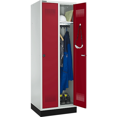 Ein offener, weiß-roter Schrank mit Arbeitskleidung. Rechts sind eine Jacke und ein Helm zu sehen, links Schuhe.