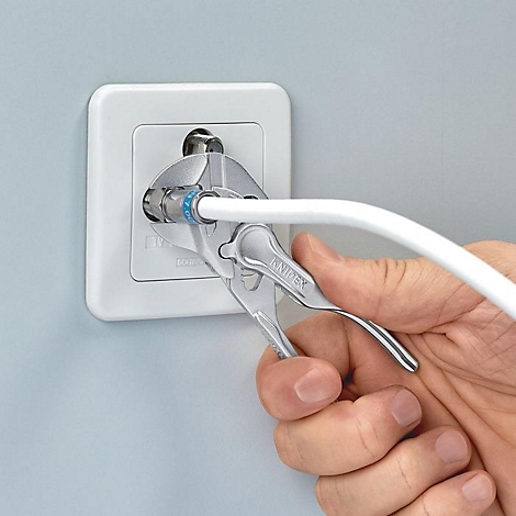 Une personne visse un câble coaxial dans une prise blanche avec une pince.