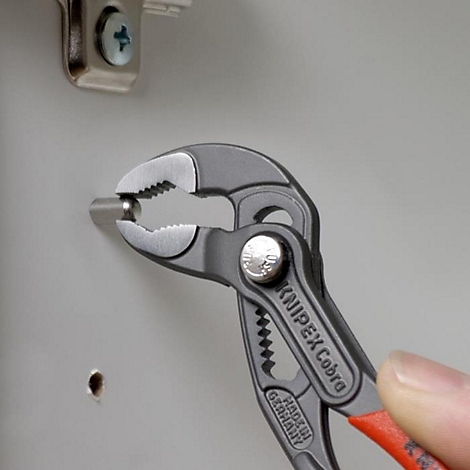 Eine Zange hält einen Stift, der in ein Loch gesteckt wird. Auf der Zange steht „KNIPEX Cobra“, rot abgesetzter Griff.
