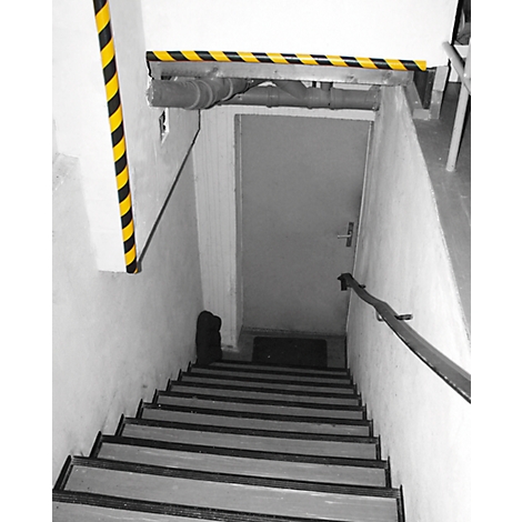 Escalera con marcas de peligro negras y amarillas, puerta gris y pasamanos.