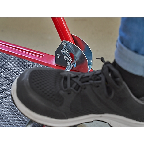 Nahaufnahme: Schwarzer Schuh auf einer roten Metallkonstruktion mit Feder und Fußstütze.