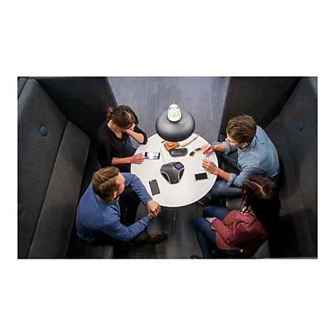 Vier Personen sitzen an einem runden Tisch in einer Nische, umgeben von dunklen Wänden. Auf dem Tisch liegen Smartphones, eine Konferenzkamera und andere Gegenstände.