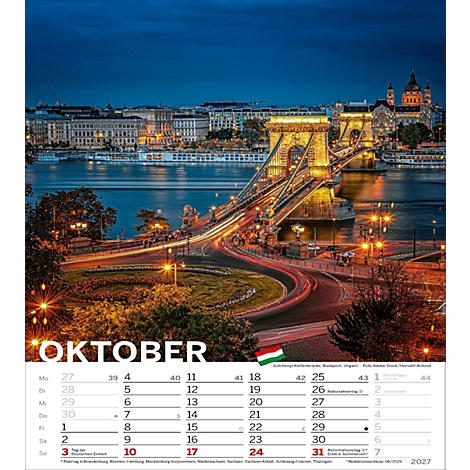 Vue sur le pont des Chaînes illuminé sur une rivière la nuit. En premier plan, le mois d'octobre. Une ville peut être vue à l'horizon.