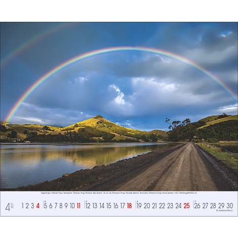 Un double arc-en-ciel surplombe un paysage avec un lac, des collines et une route.