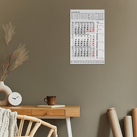 Un calendrier mural avec des dates quotidiennes, accroché au mur. Un vase, une horloge et une tasse sont sur un bureau.