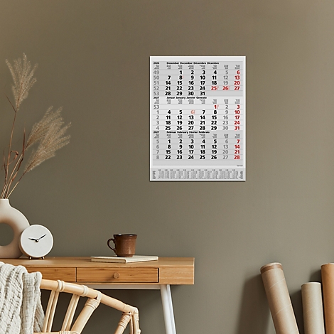 Un calendrier mural avec des dates et des chiffres en rouge et noir. Un bureau avec des décorations est visible au premier plan.