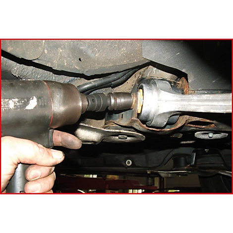 Ein Mechaniker verwendet einen Schlagschrauber, um ein Fahrwerksteil an einem Fahrzeug zu lösen.