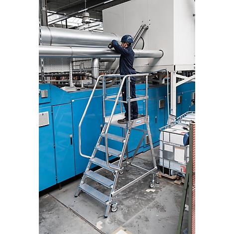 Een arbeider staat op een zilveren trap, pijpen te repareren. Blauwe fabrieksapparatuur op de achtergrond.