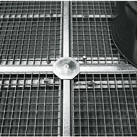 Draufsicht auf einen Metallrost mit achteckiger Abdeckung in der Mitte. Der Rost ist in Quadrate unterteilt.