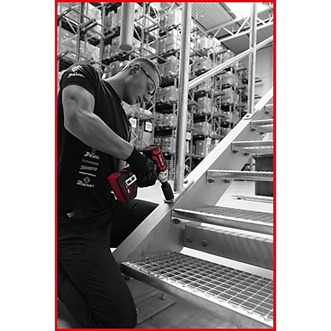 Handwerker in einem Lager verschraubt mit einem rot-schwarzen Schlagschrauber eine Metalltreppe.