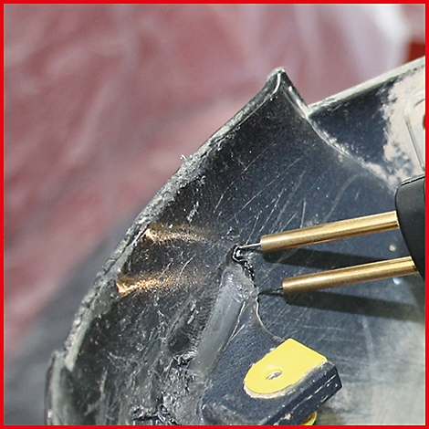 Nahaufnahme eines Kunststoffschweissgeräts, das eine Metallklammer zur Reparatur eines schwarzen Kunststoffteils erhitzt.