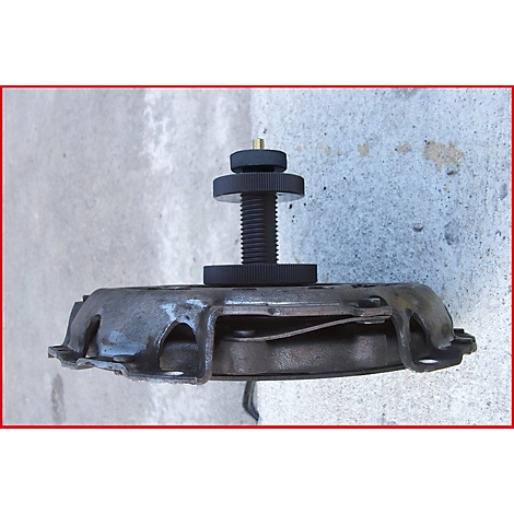 Graue Kupplung mit schwarzem Werkzeug auf Beton. Schraube mit Rändelrad, umgeben von metallischen Elementen.