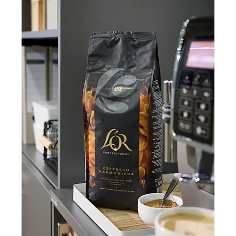 Eine Packung L'OR Professional Espresso Harmonieux auf einem Tablett. Daneben eine Kaffeemaschine und Kaffeepulver.