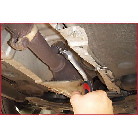 Ein Mechaniker löst eine Schraube an einem Auspuffrohr mit einer Ratsche. Die untere Fahrzeugseite ist zu sehen.