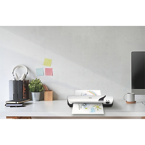 Een printer print een kindertekening op een witte tafel. Daarnaast staan een koptelefoon, notitieboeken en een monitor.