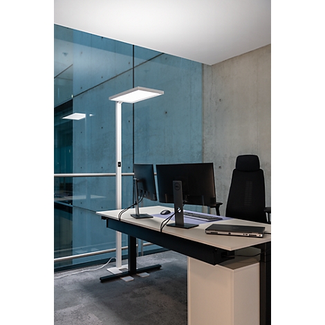 Bureau avec bureau, moniteurs, lampe, chaise, mur gris et fenêtre.