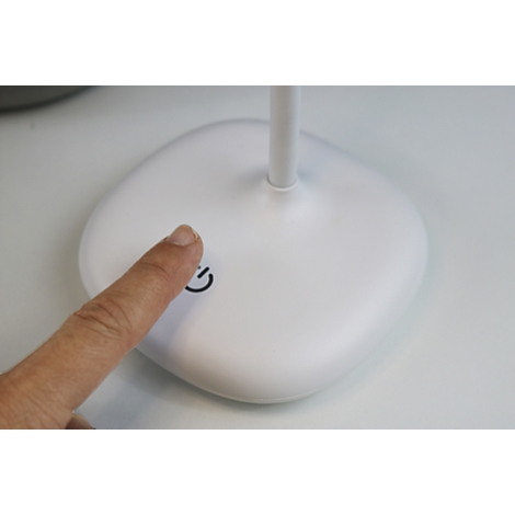 Un doigt touche l'interrupteur marche/arrêt d'une lampe de bureau blanche.