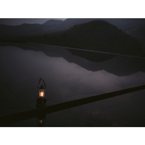 Lampe noire et blanche avec un couvercle en verre transparent et une base en bois, ornée d'une poignée tressée.