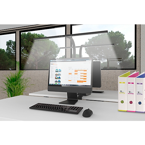 Un espace de travail avec moniteur, clavier et dossiers. En arrière-plan, des fenêtres avec vue sur la verdure.