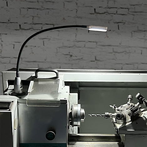 Lampe de travail LED noire sur un tour à métaux. La lampe éclaire la pièce à usiner.