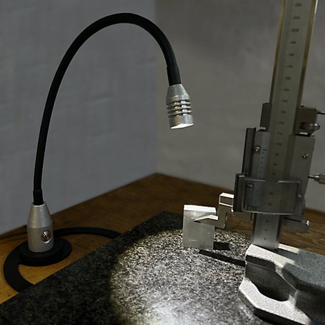 Une lampe de travail lumineuse éclaire des outils de mesure sur un établi. L'accent est mis sur un comparateur à cadran.