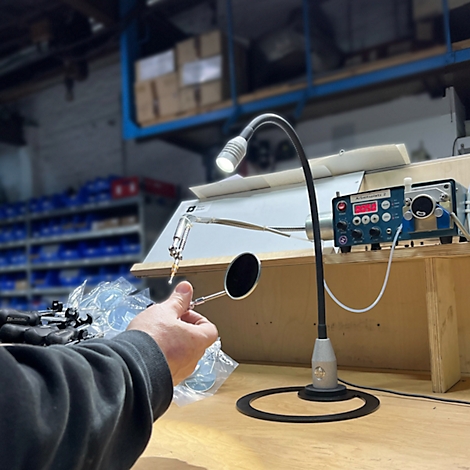Une main tient un petit miroir rond devant une lampe. Un appareil de mesure est en arrière-plan.