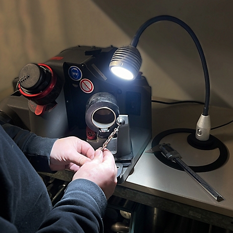 Une personne tient une pièce devant une machine-outil, éclairée par une lampe.