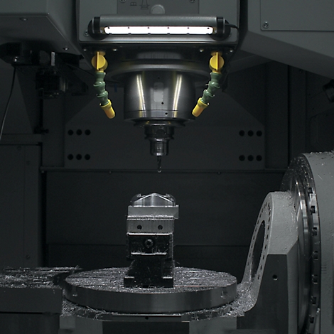 Machine-outil en cours d'utilisation : fraisage d'une pièce métallique, liquide de refroidissement, éclairage.