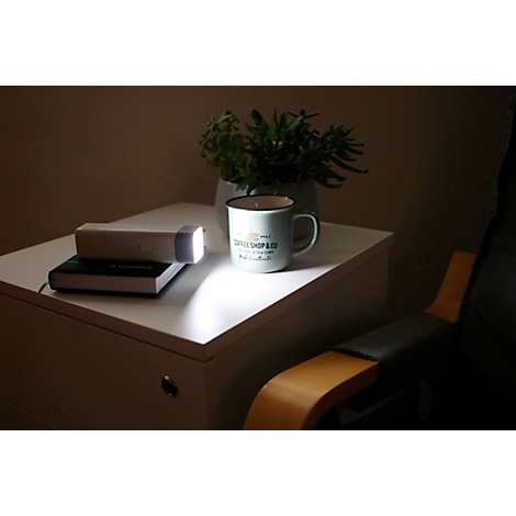 Une table de chevet blanche avec lampe, livre, tasse et plante. Un cône de lumière illumine la scène.