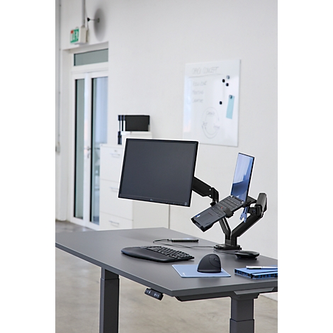 Schreibtisch mit Monitor, Laptop und Peripheriegerät. Helle Büroumgebung. Der Monitor und der Laptop sind auf Halterungen befestigt.