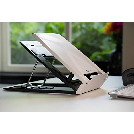 Witte laptopstandaard op een bureau, raam en bloemenvaas op de achtergrond.