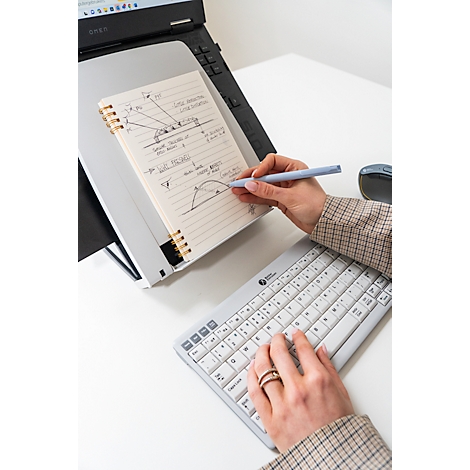 Persoon schrijft aantekeningen in een notitieboekje terwijl ze op een computer werkt.