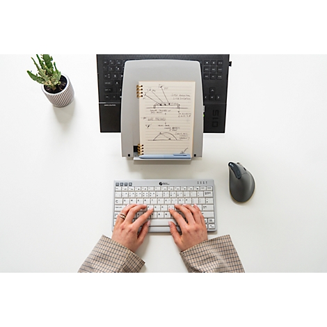 Bovenaanzicht van een persoon die op een toetsenbord typt. Daarnaast een muis, notitieblok en een plant.