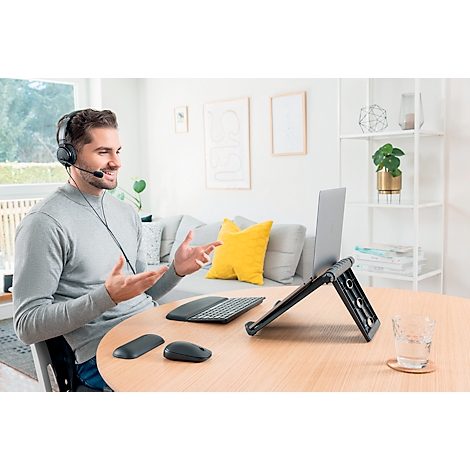 Een man met een headset, laptop en accessoires tijdens een videogesprek. Hij gebaart en lacht. Op de tafel staan een laptop, muis, toetsenbord en een glas.